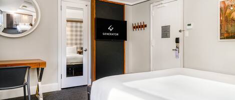 A hotel room with a large bed, a desk, a chair, a mirror, a television, and a door.
