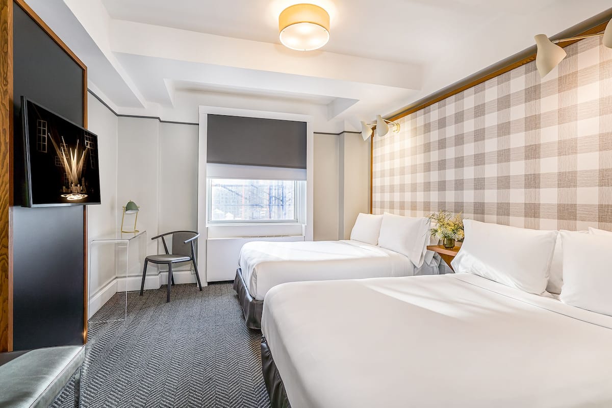 Quarto de hotel com duas camas, televisão, janela e cabeceira xadrez.
