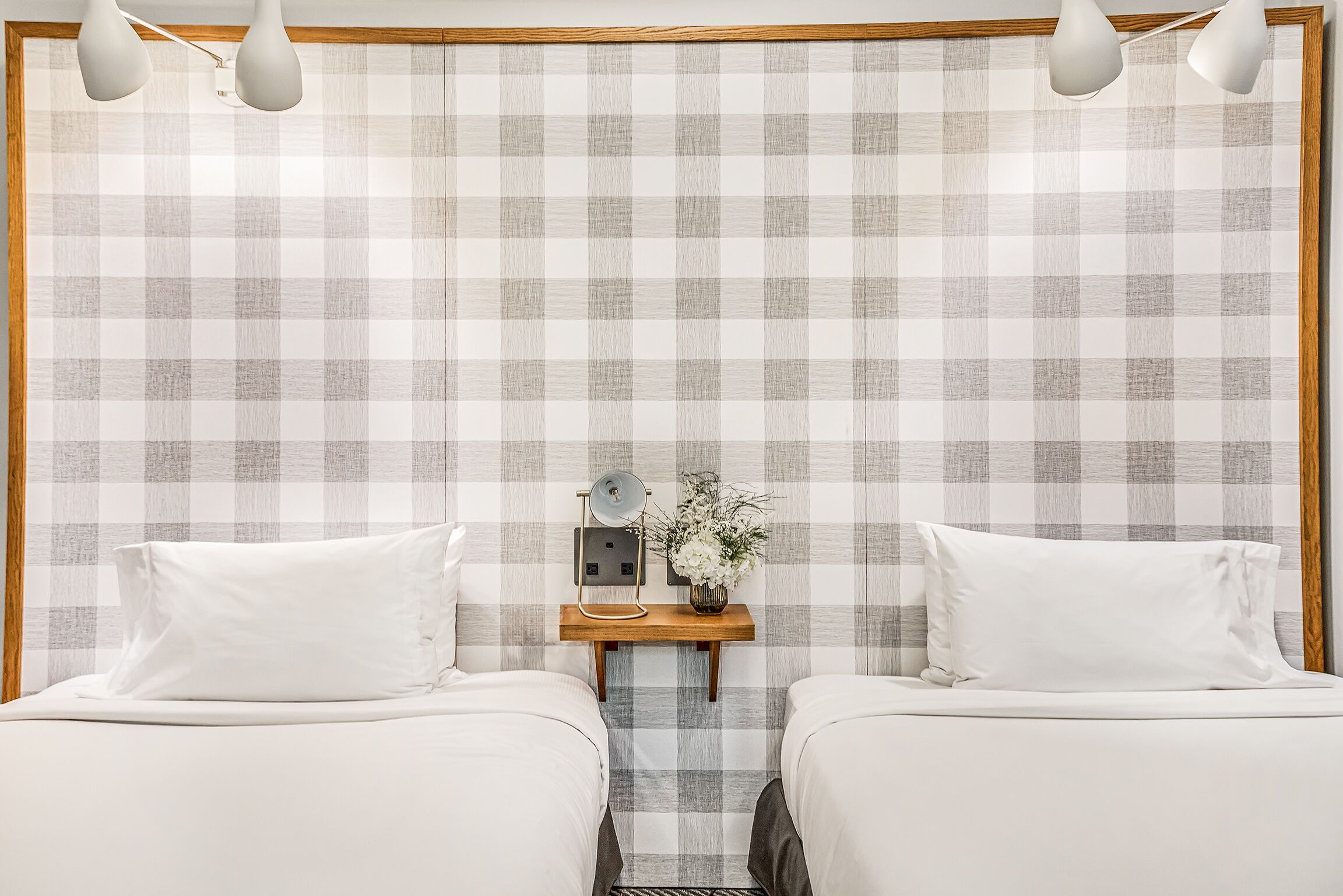 A bedroom with two beds, a nightstand with a lamp, and a wall with a checkered pattern.