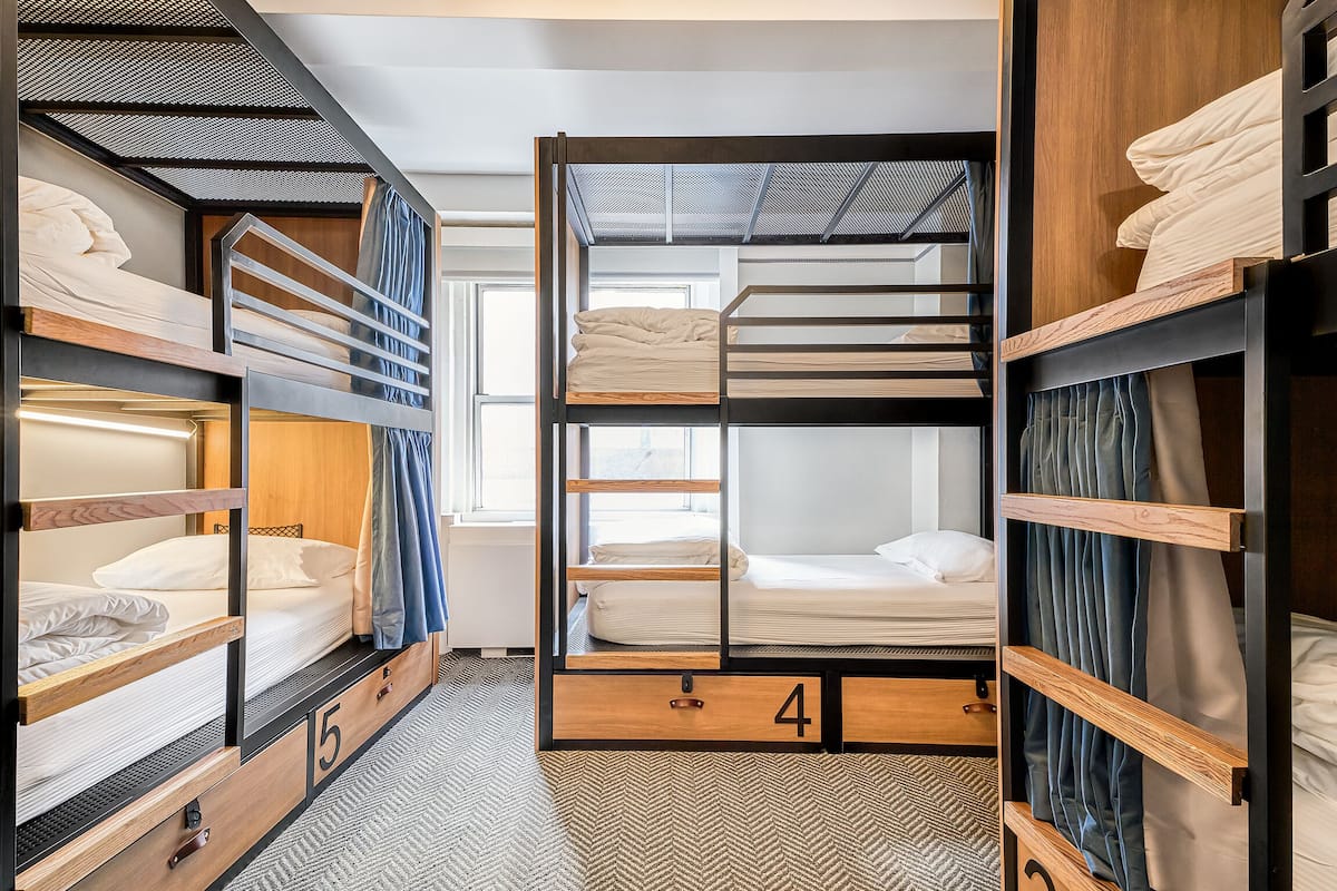 Quarto em dormitório compacto e moderno, com beliches, unidades de armazenamento em madeira e piso com padrão herringbone.