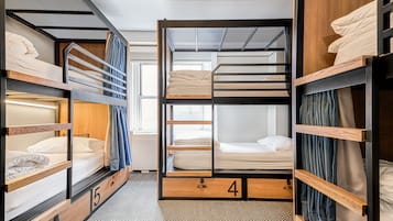 Quarto em dormitório compacto e moderno, com beliches, unidades de armazenamento em madeira e piso com padrão herringbone.