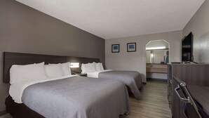 A hotel room with two beds, a dresser, a mirror, and a television.