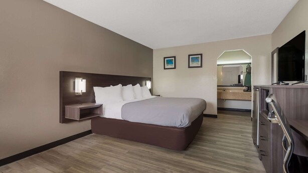 A hotel room with a bed, a desk, a mirror, and a TV.