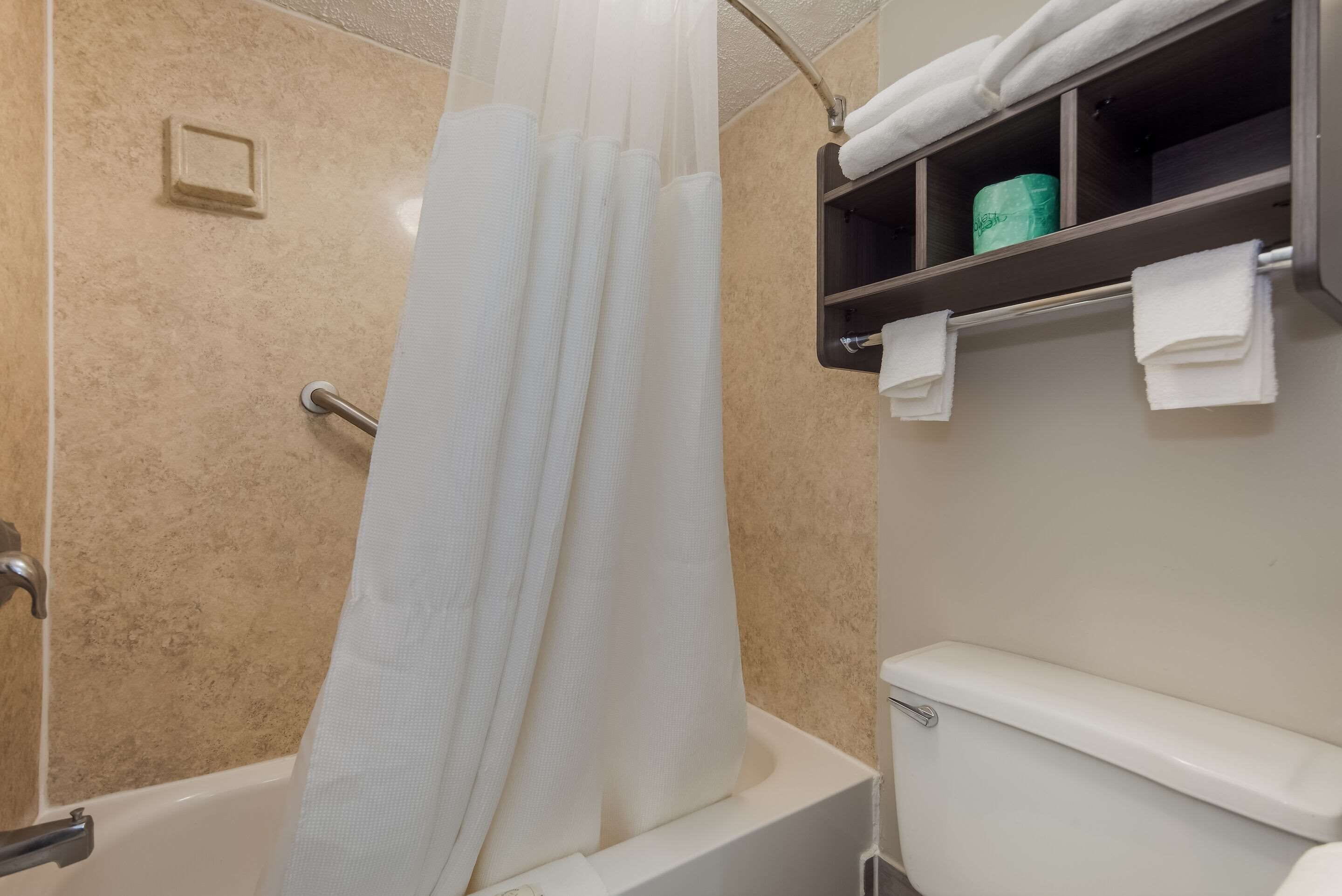 A bathroom with a bathtub, a toilet, a towel rack, and a shelf with towels and a green bottle.