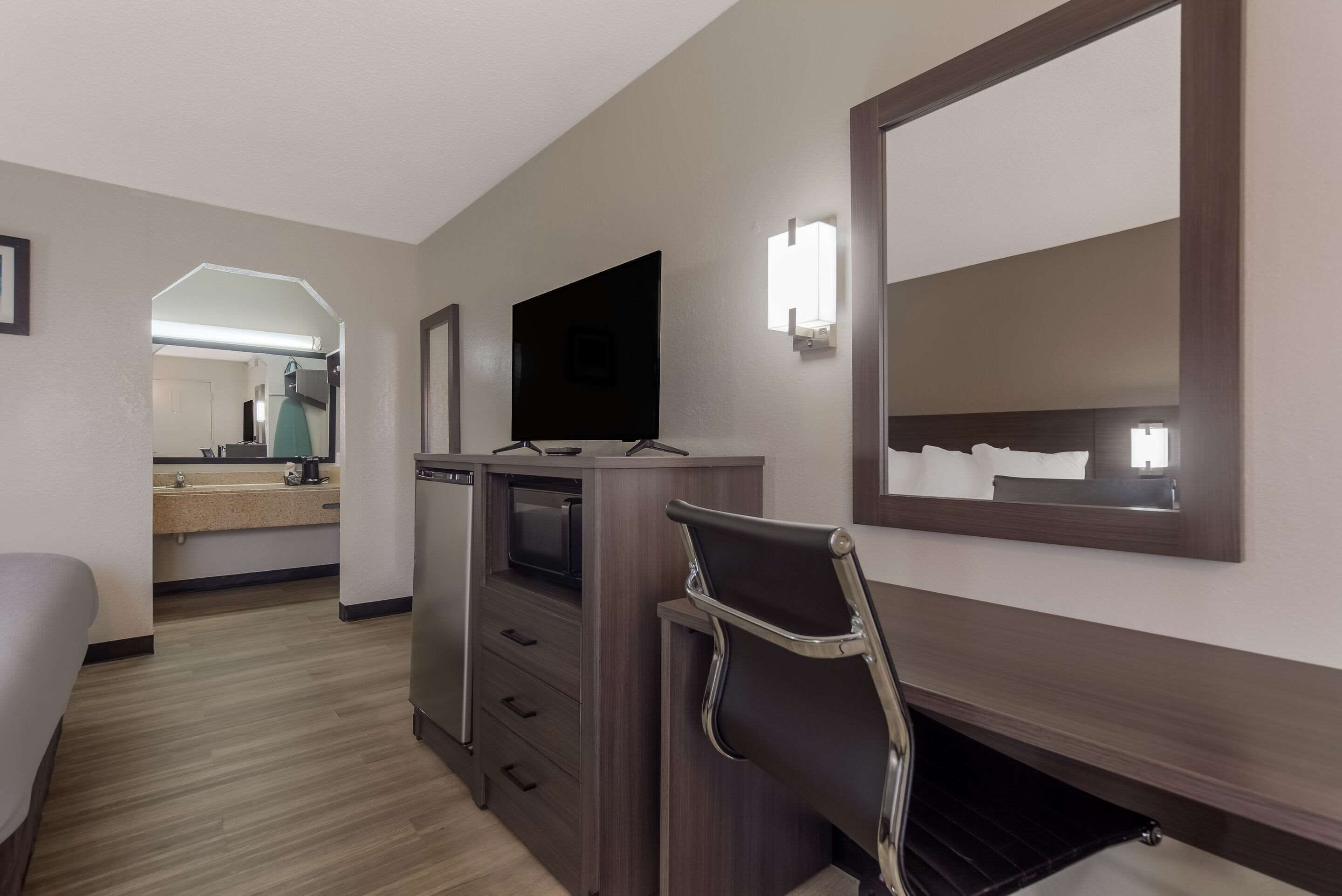 Une chambre d’hôtel équipée d’un lit, d’une télévision, d’un bureau avec des tiroirs, d’un miroir et d’un four à micro-ondes.