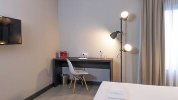 Une chambre d’hôtel comprenant un lit, un bureau avec une chaise, une lampe de bureau, un téléviseur et une fenêtre avec des rideaux.