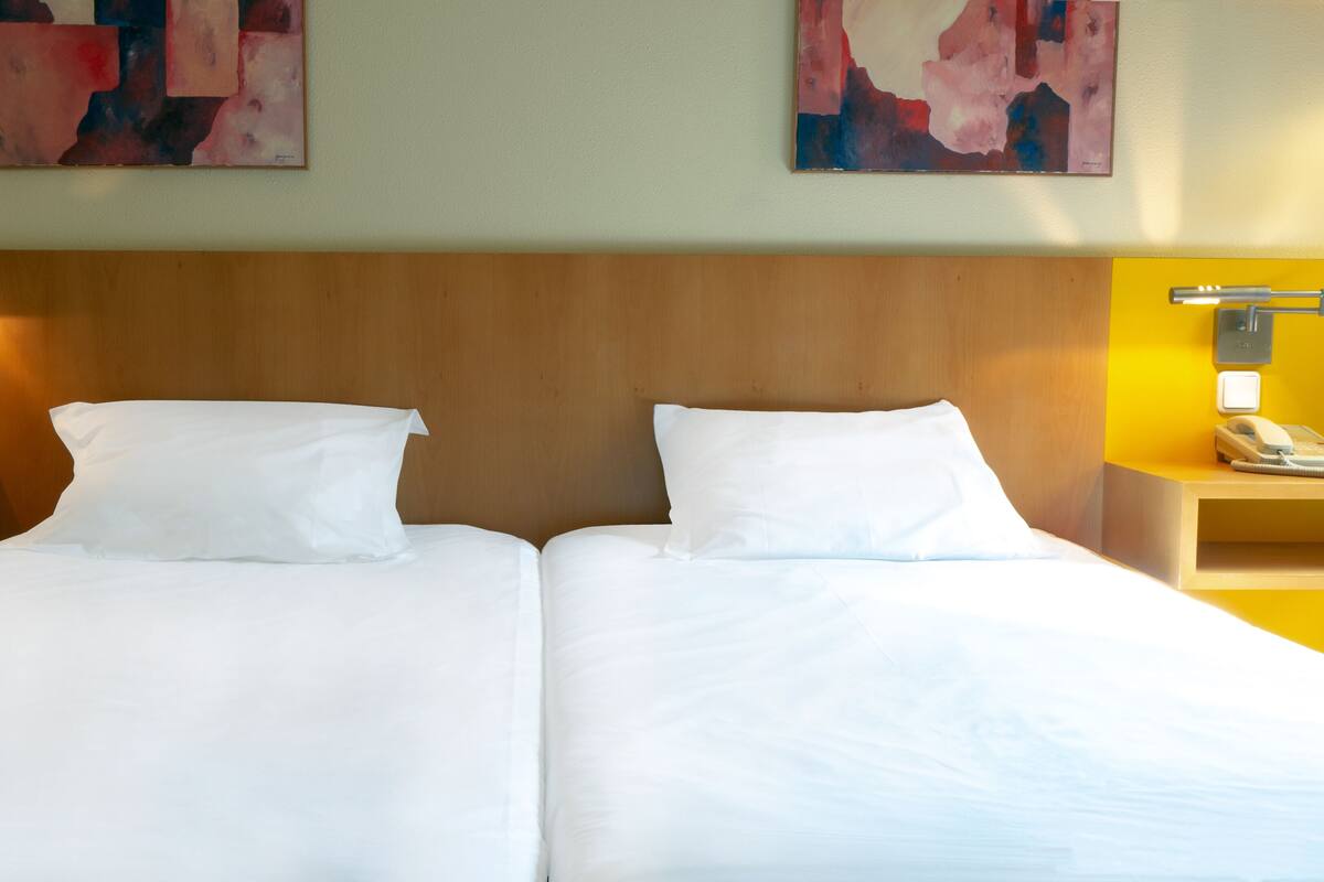 A double bed with white linens, wooden headboard, bedside tables with lamps, and abstract paintings on the wall.