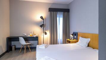 A hotel room with a large bed, a desk, a chair, a lamp, and a window with curtains.