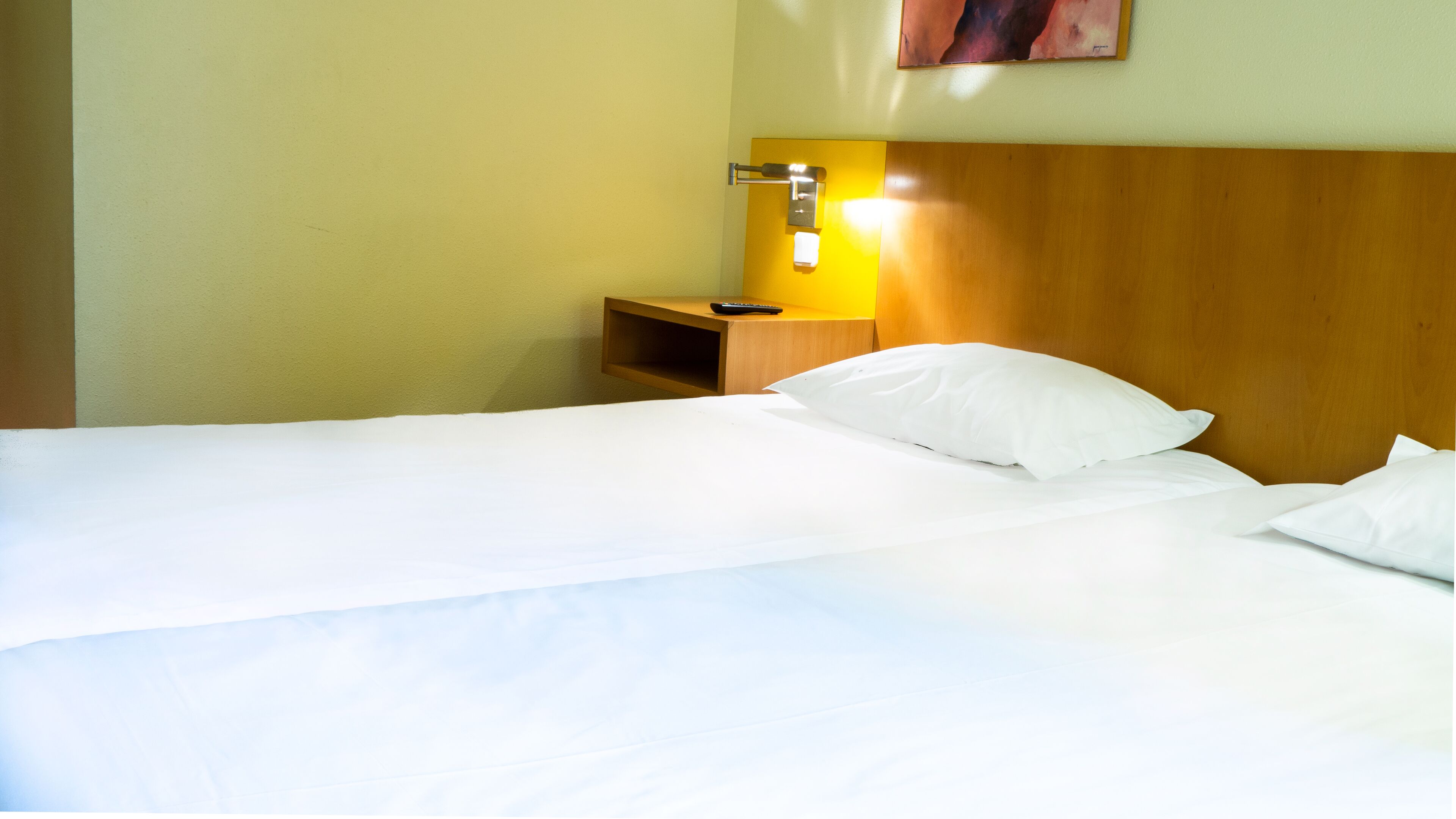 Una habitación de hotel con cabecera de madera, una mesita de noche con control remoto y una lámpara de pared.