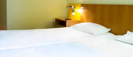 Una habitación de hotel con cabecera de madera, una mesita de noche con control remoto y una lámpara de pared.
