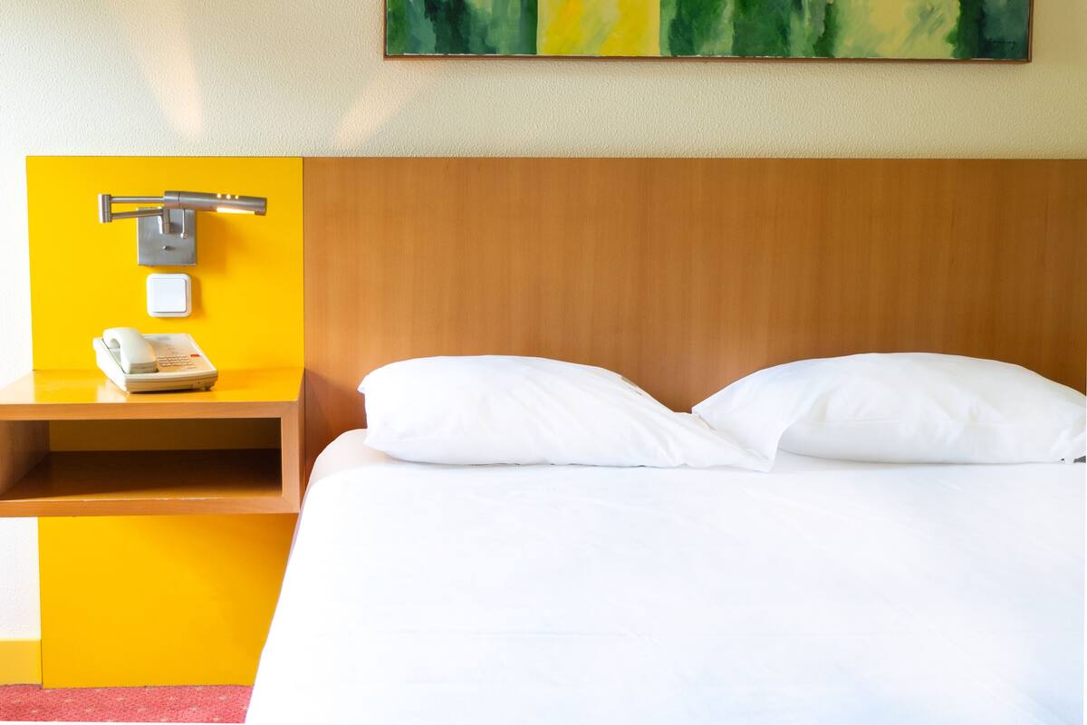 A hotel room with a wooden headboard, a bedside table with a telephone, and a painting on the wall.