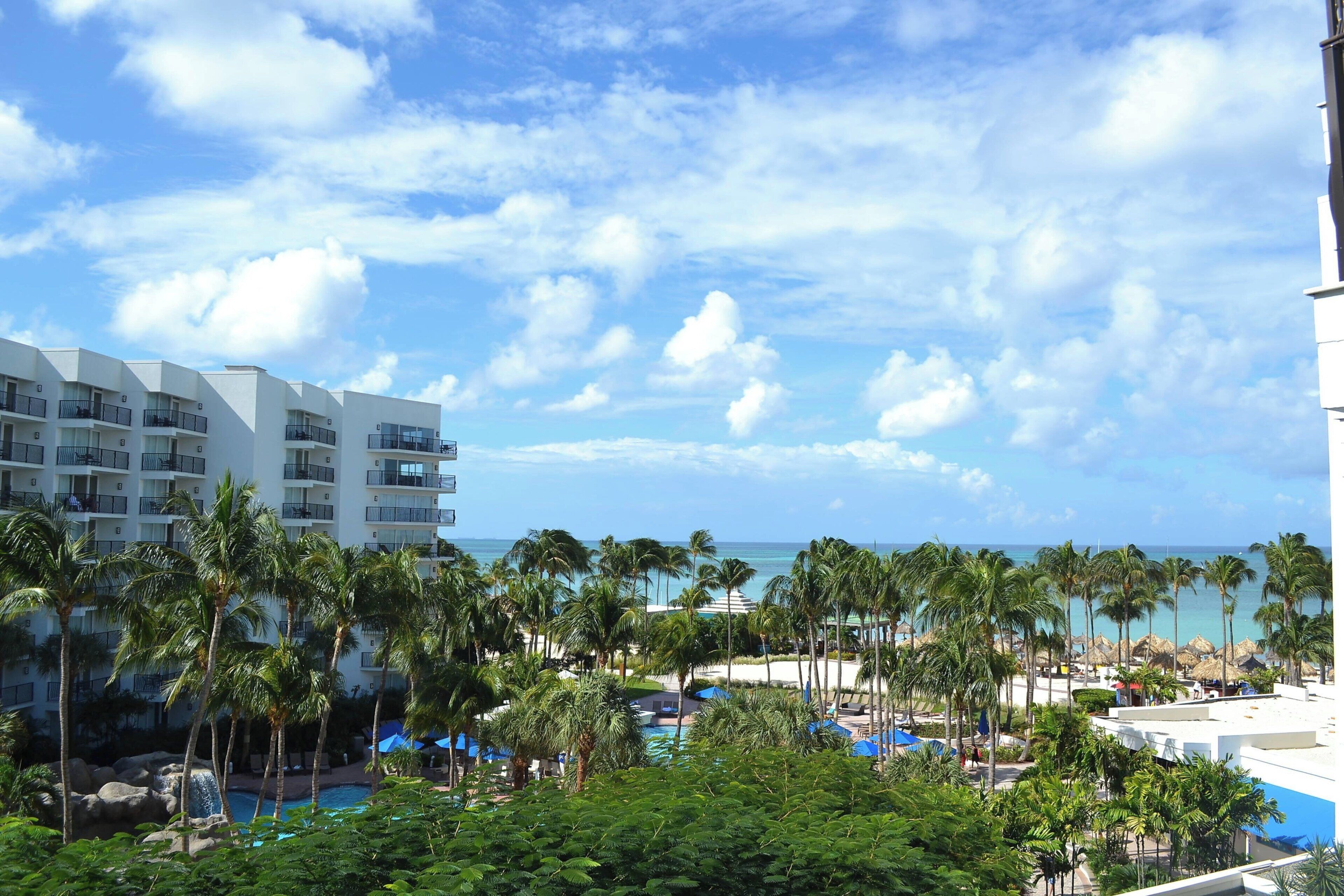 A resort with a pool, palm trees, and a view of the ocean.