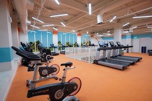 A gym with treadmills, stationary bikes, and elliptical machines, featuring a high ceiling with exposed beams and bright lighting.