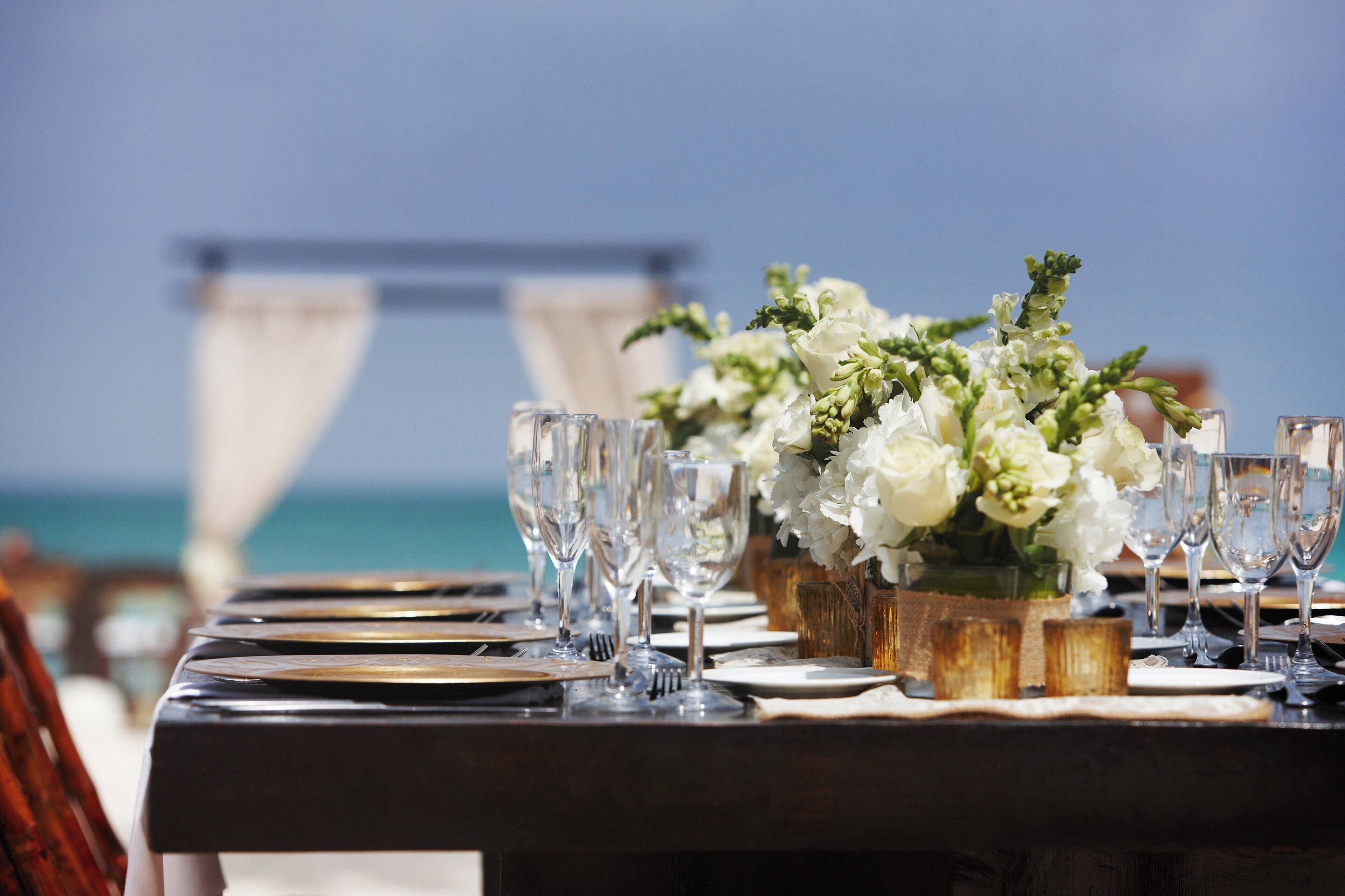 A table set for a meal with glasses and a floral centerpiece, overlooking a body of water.