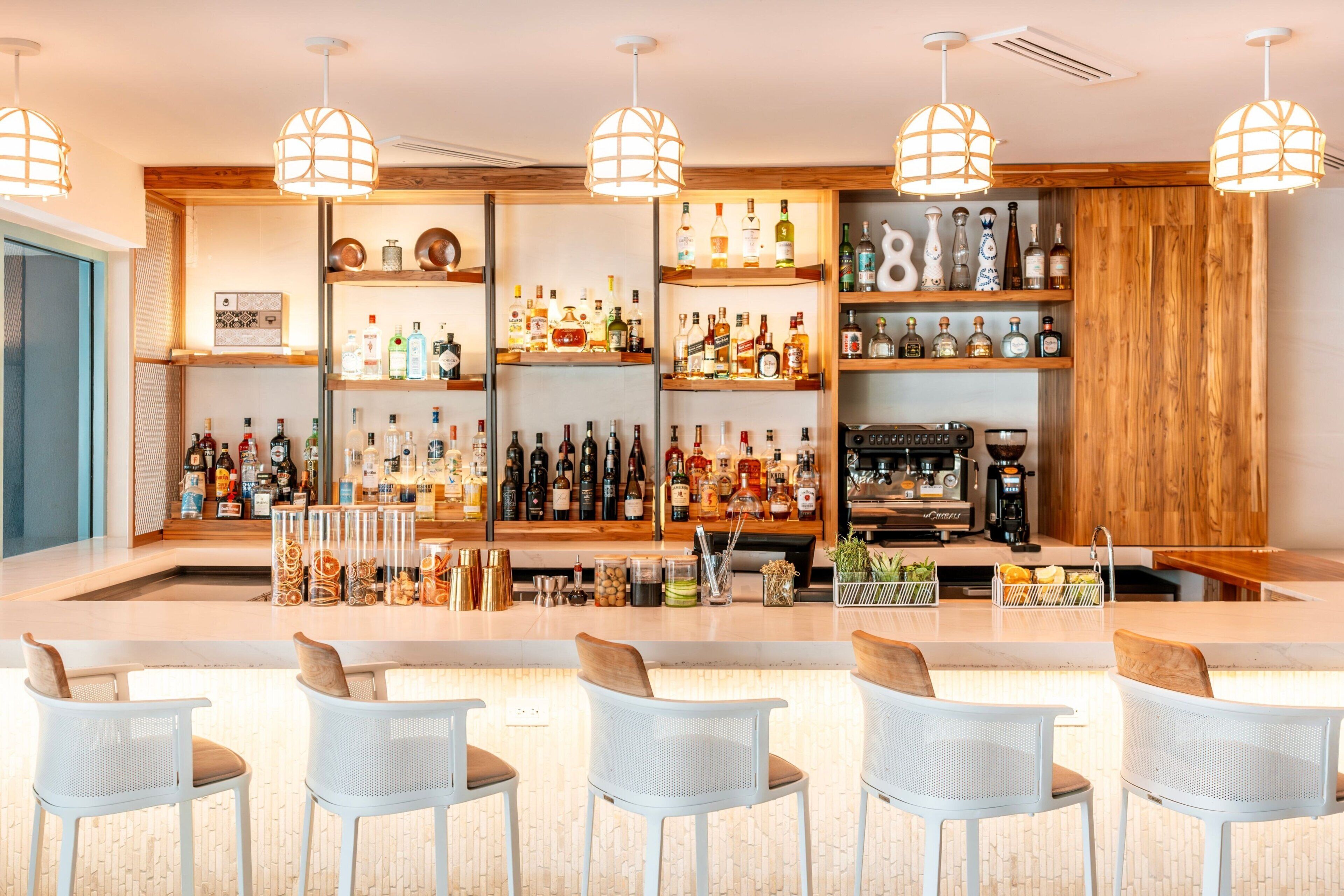 Zona de bar con varias estanterías llenas de botellas de licor, una máquina de café y taburetes.