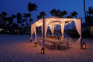 A beachside tent with string lights, a table set for dining, and palm trees in the background. - Aruba Marriott Resort & Stellaris Casino (Noord)