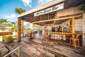 A beach bar with a rustic wooden exterior, outdoor seating, and a sign indicating its location.