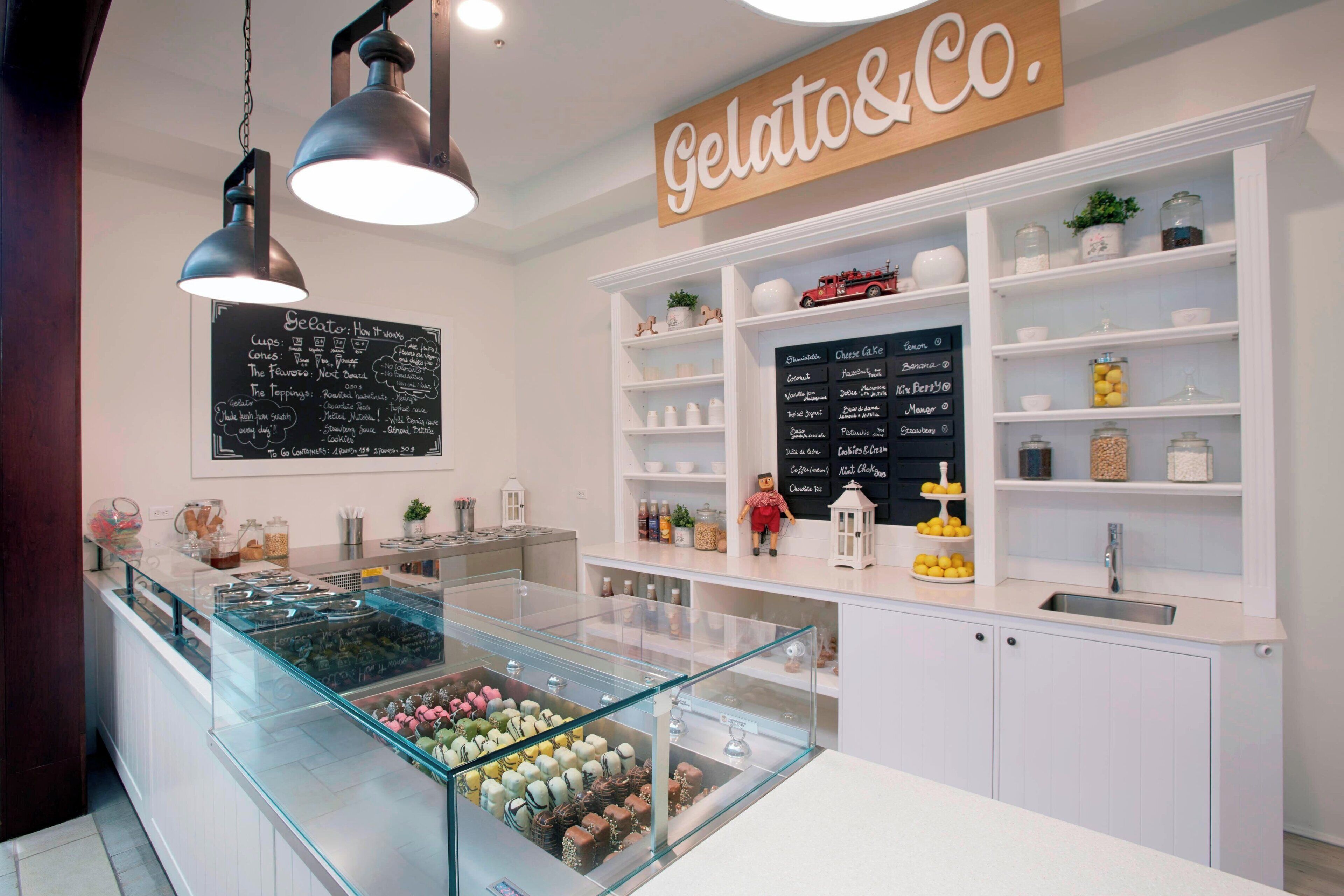 L’intérieur d’un magasin de glaces artisanales, avec un présentoir rempli de différentes sortes de glaces, un tableau noir servant de menu et des  étagères où sont exposés des bocaux et des ustensiles de cuisine.