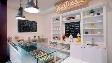 A gelato shop interior with a display case of gelato, a chalkboard menu, and shelves with jars and kitchen items.