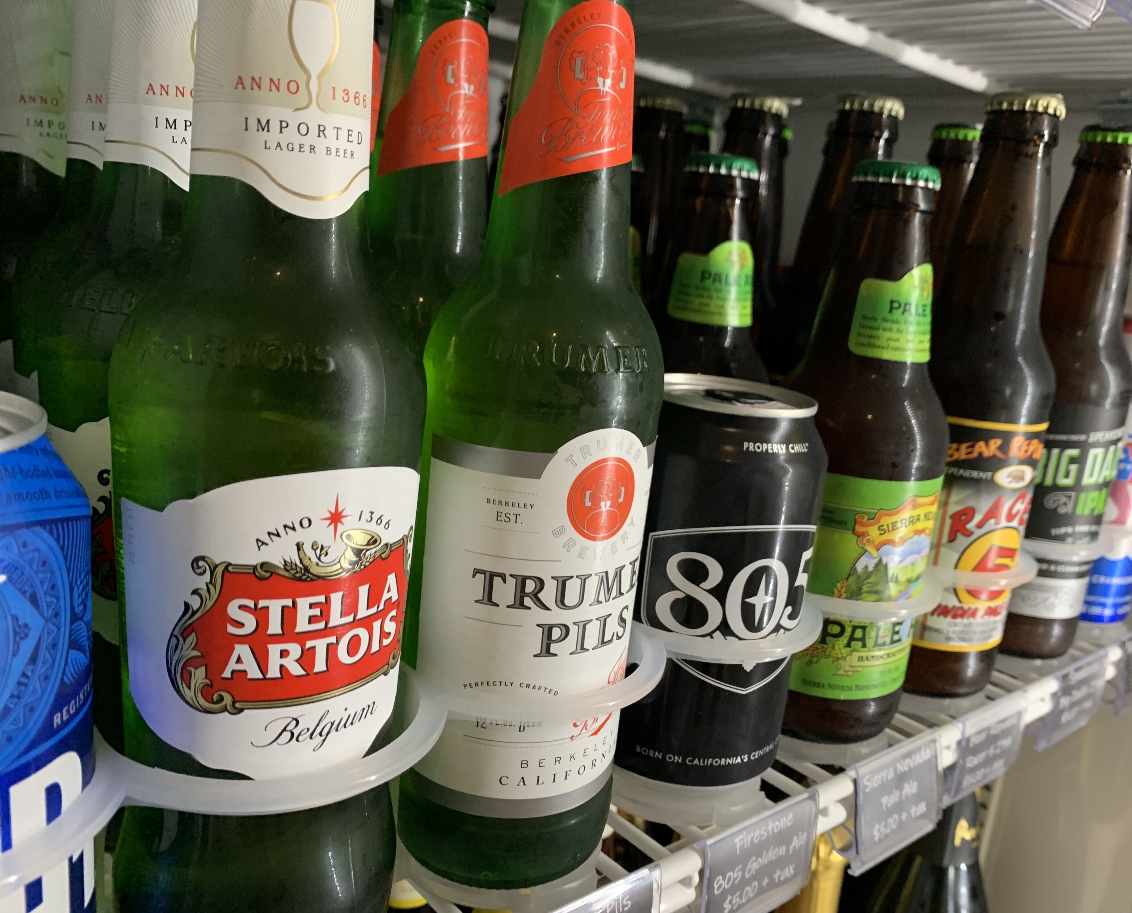 Une étagère remplie de différentes bouteilles et canettes de bière, notamment des marques comme Stella Artois et Trumpel.