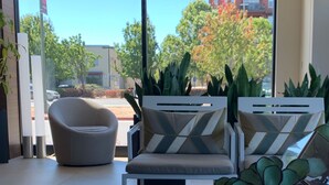 A modern interior with two armchairs, a coffee table, and a large window offering a view of the street and buildings outside.