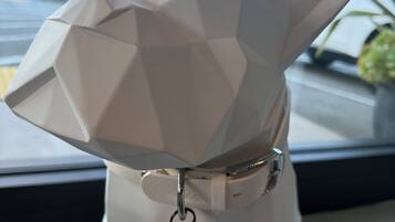 Eine weiße, geometrische Hundefigur mit einem Anhänger am Halsband.
