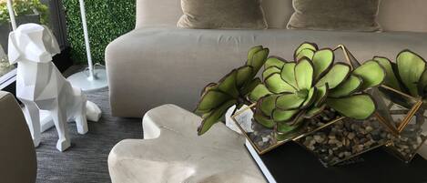 Un salon moderne avec un canapé, une sculpture géométrique blanche, une plante dans un vase géométrique et un livre intitulé « LE LIVRE DES VILLES ».