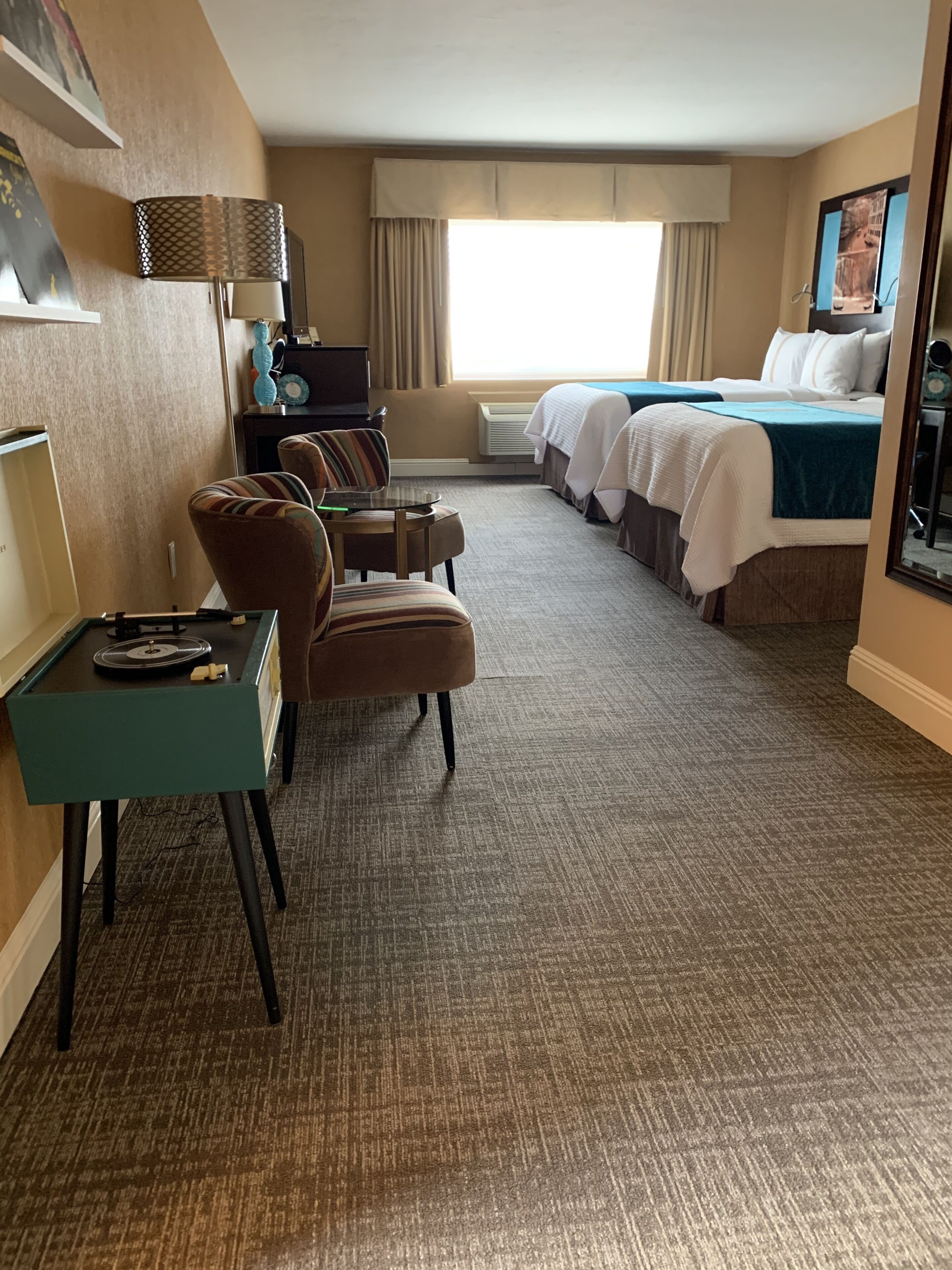 A hotel room with a bed, two armchairs, a small table, and a desk with a lamp.
