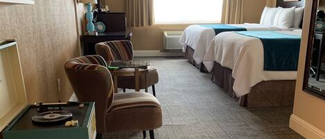A hotel room with a bed, two armchairs, a small table, and a desk with a lamp.