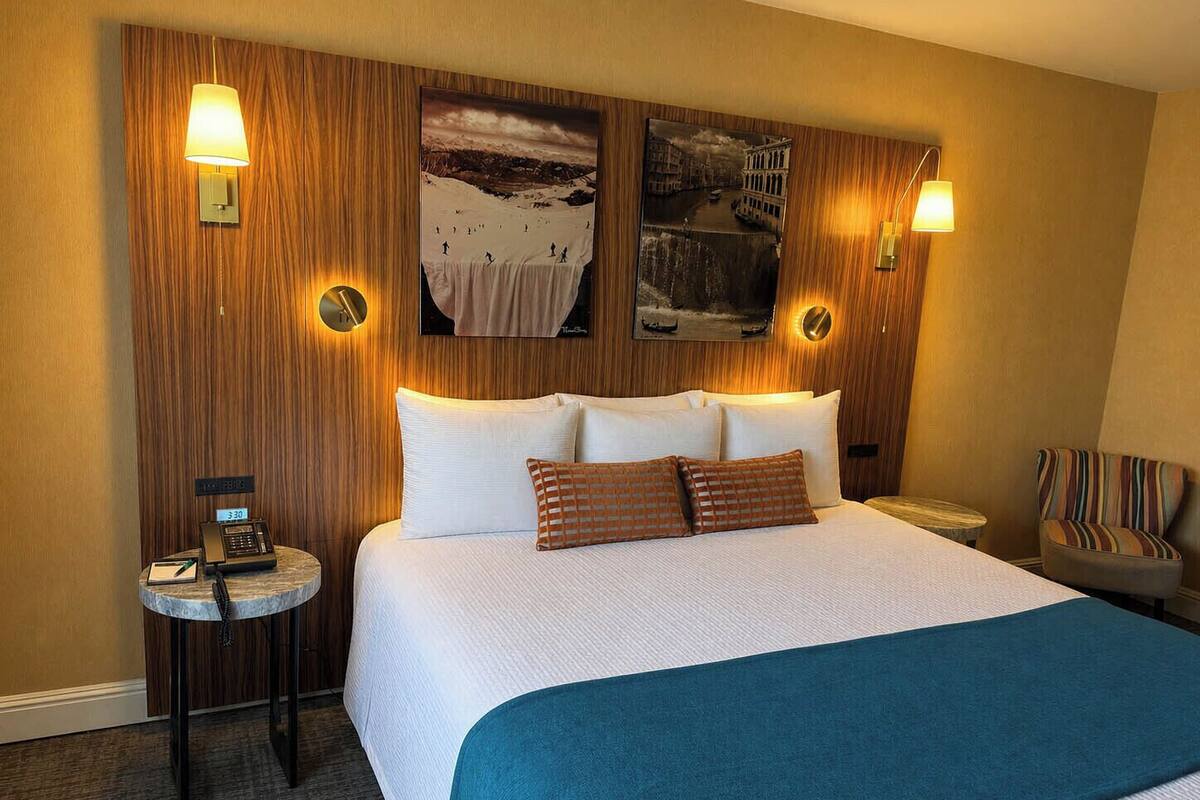 A hotel room with a large bed, two wall-mounted lamps, a small side table with a phone, and a chair.