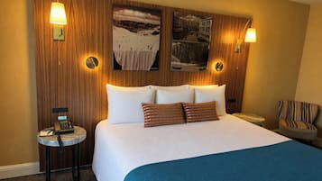 A hotel room with a large bed, two wall-mounted lamps, a small side table with a phone, and a chair.