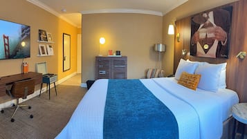 Una habitación de hotel con una cama, un escritorio, una silla, un televisor y un cuadro grande en la pared.