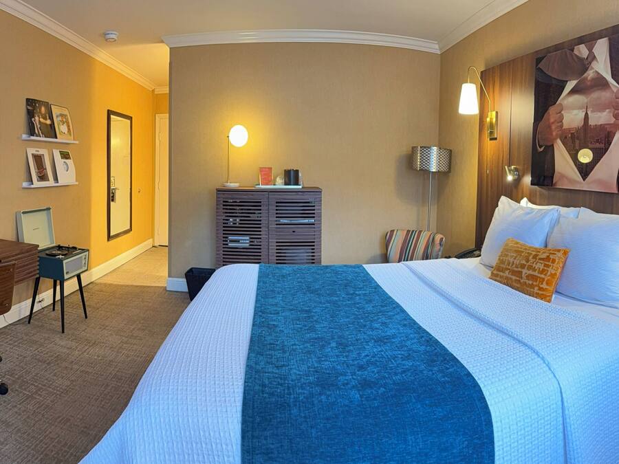 Una habitación de hotel con una cama, un escritorio, una silla, un televisor y un cuadro grande en la pared.