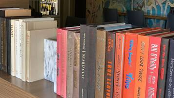Een boekenplank met verschillende boeken, een marmeren oppervlak en een achtergrond met een muur en een plank vol flessen.