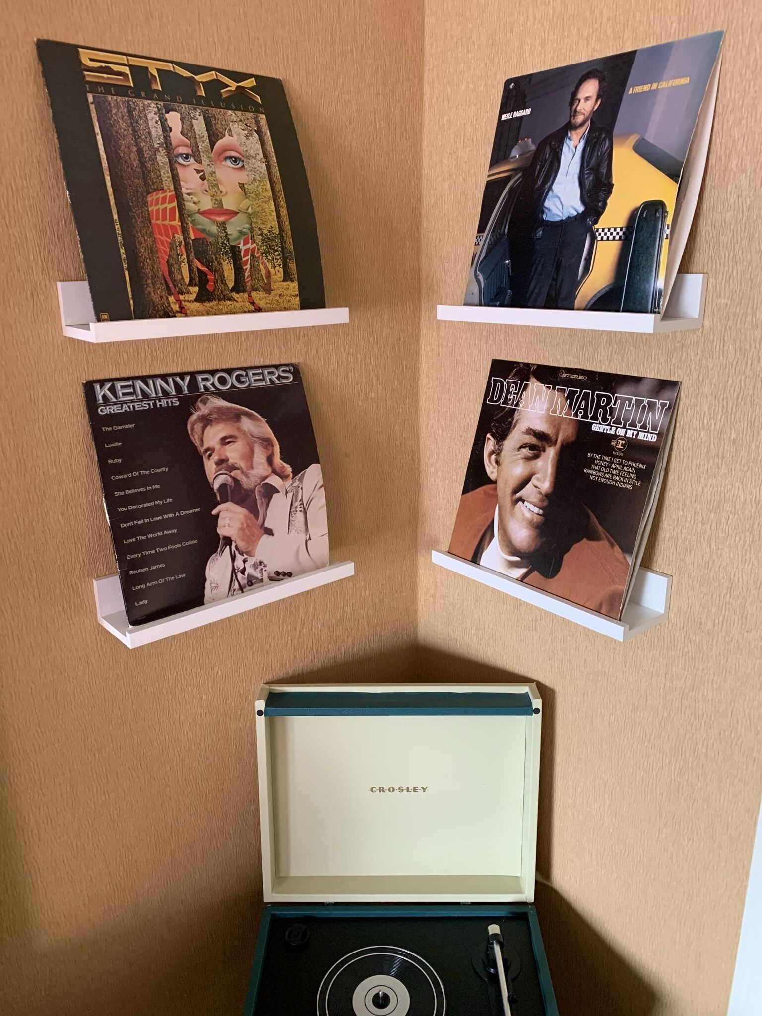 Una pared con cuatro discos de vinilo exhibidos en estanterías blancas.
