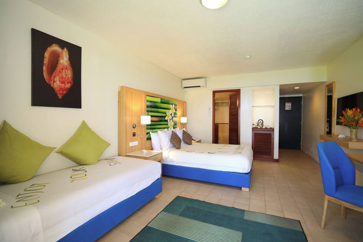 Habitación de hotel con dos camas, un escritorio y una silla. Hay un cuadro en la pared y una puerta que da a otra habitación.
