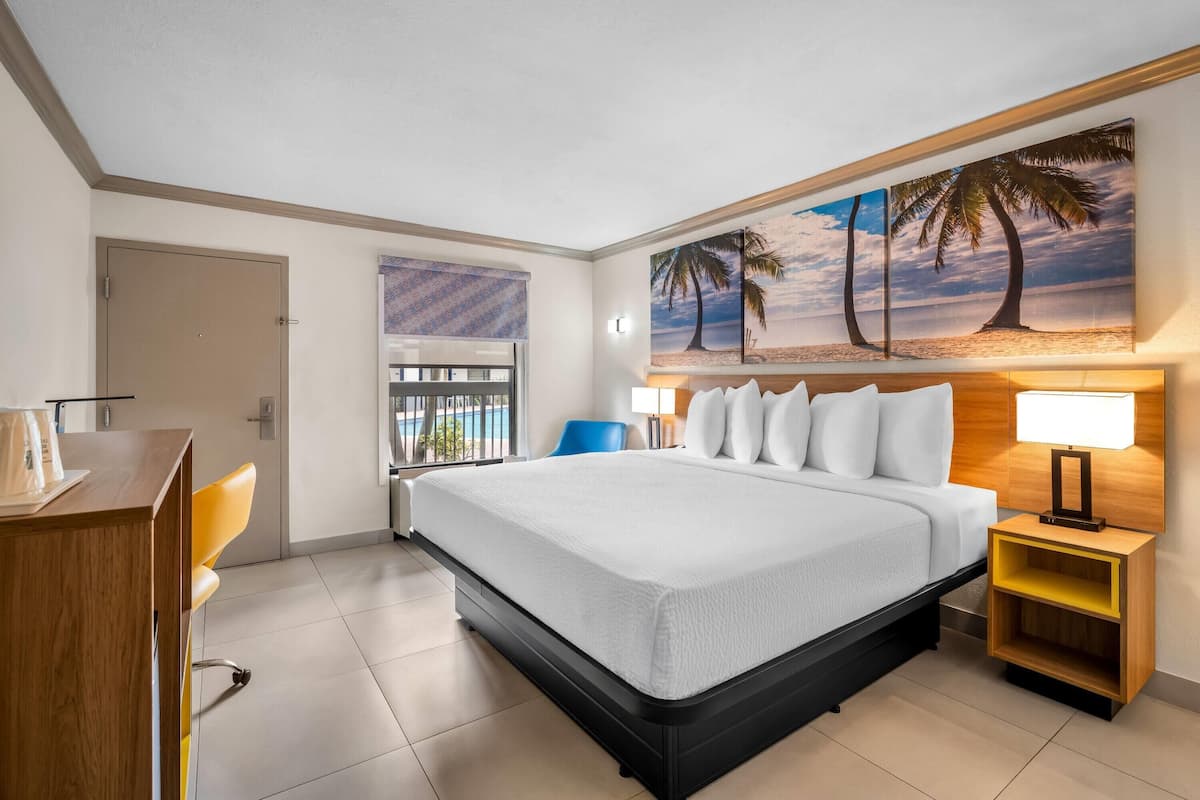 A hotel room with a bed, a desk, a chair, a nightstand, and a painting of a beach scene.