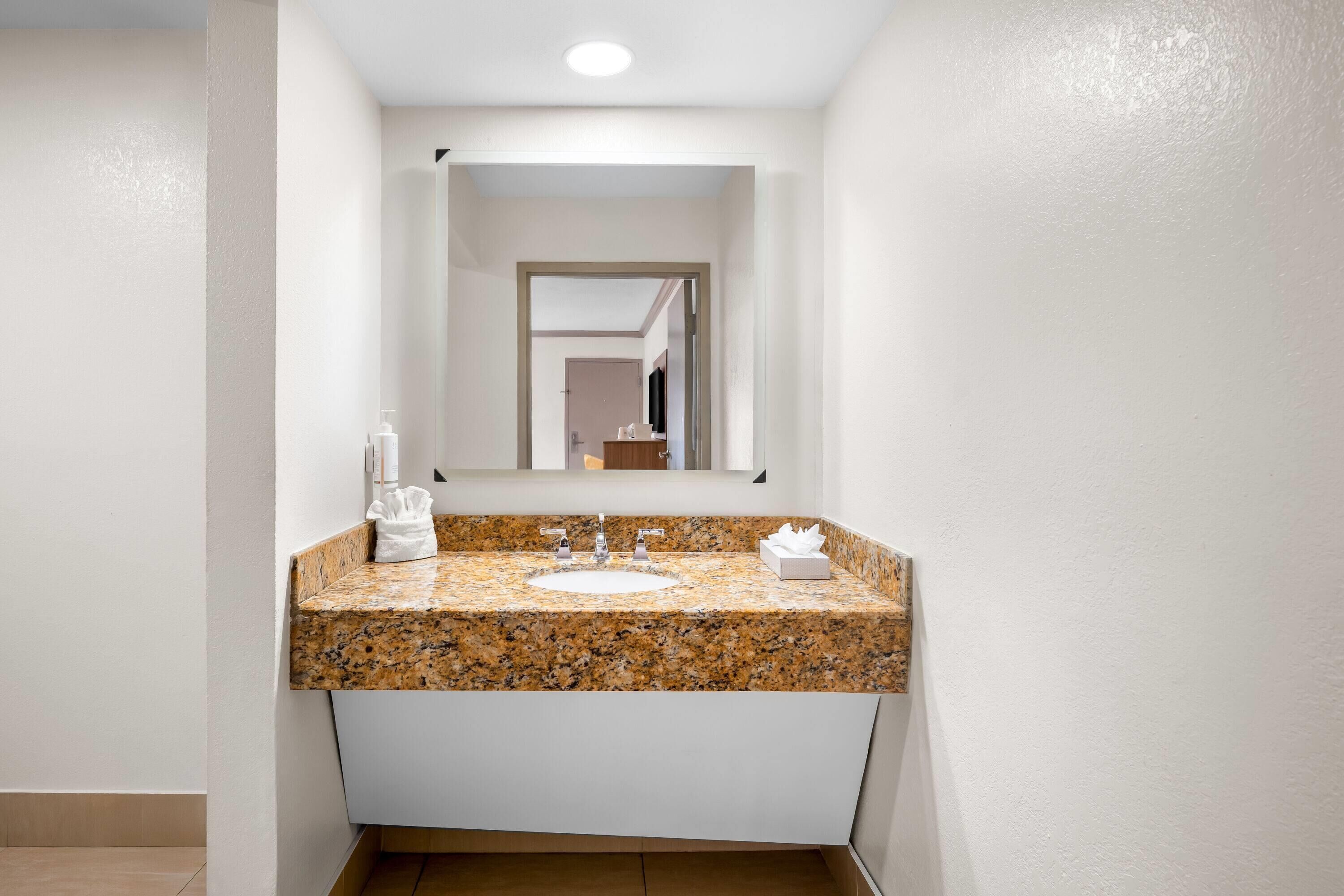 A bathroom with a granite countertop sink, a mirror, and a towel rack.