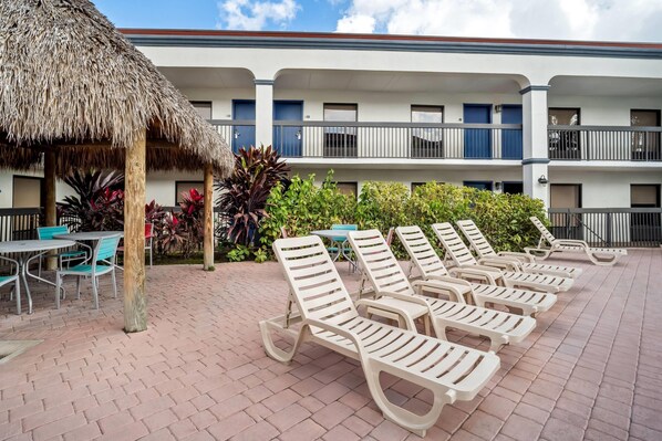 A hotel courtyard with lounge chairs, a thatched umbrella, and a poolside area.