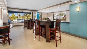 A restaurant with a bar area, high chairs, and a view of parked cars and greenery outside. - Days Inn by Wyndham Florida City (Florida City)