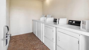 A hotel reception area with a white reception desk, a digital screen, and a small seating area.