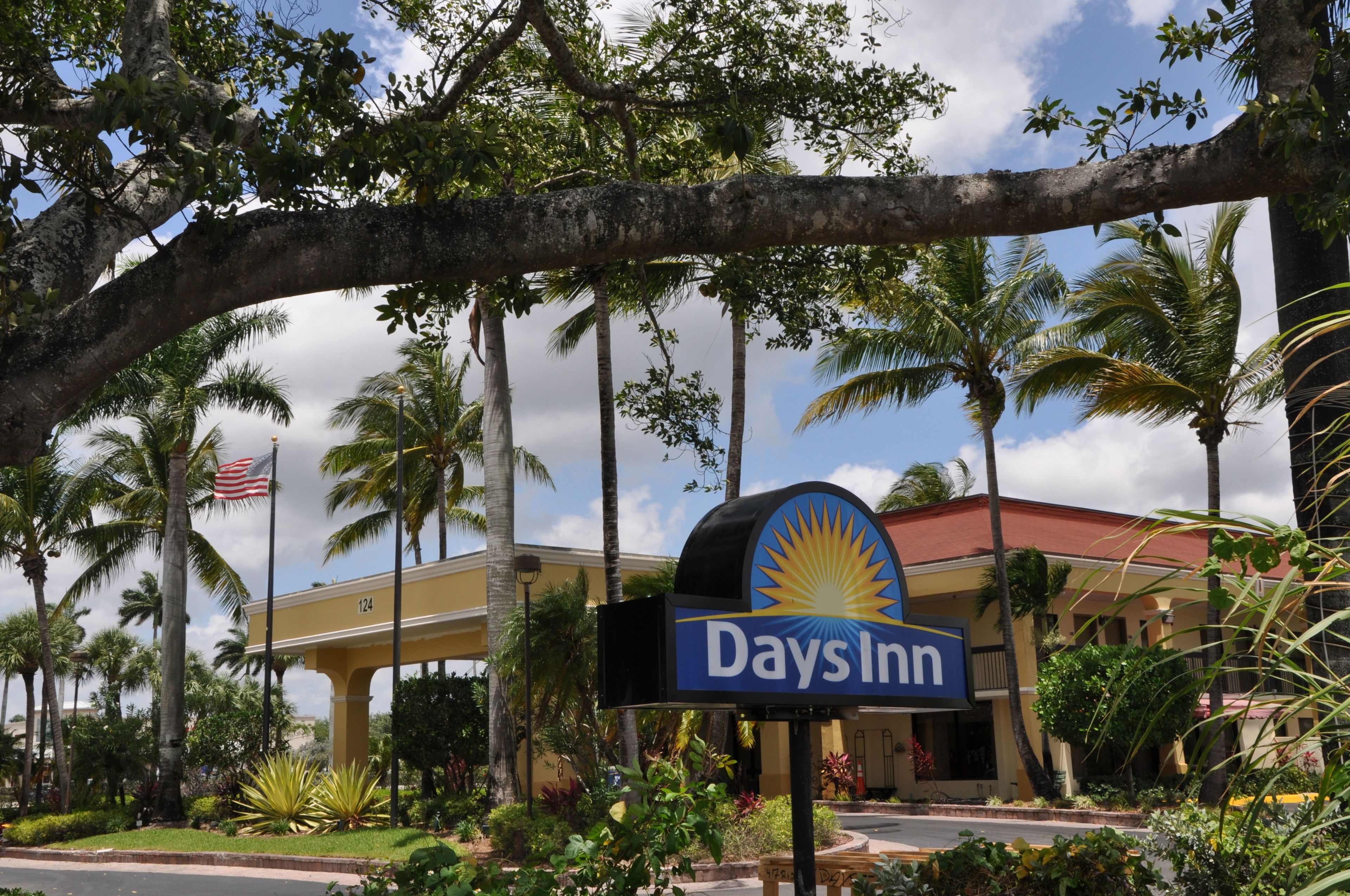 Señal de Days Inn con un logo de sol, rodeada de palmeras y cielo despejado.