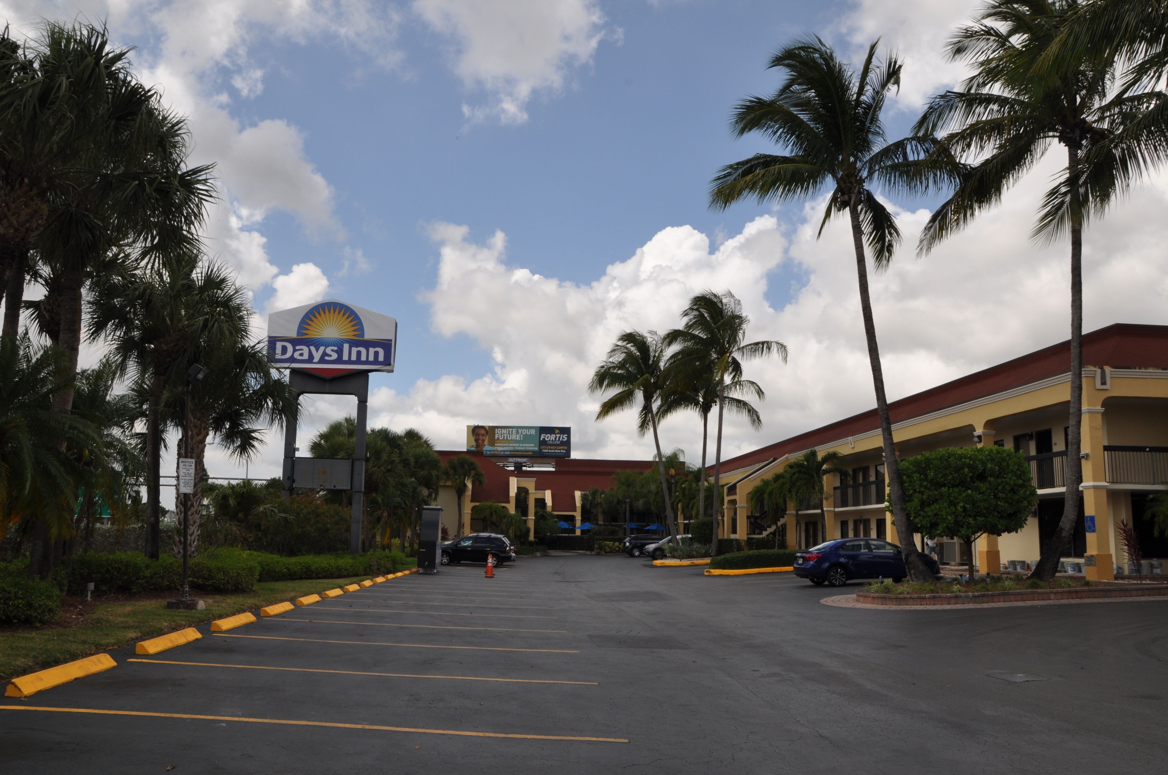 A Days Inn parking lot with palm trees and a clear sky.