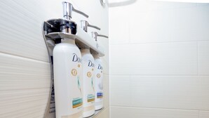 A bathroom with a white tiled wall and a shelf holding three Dove body care products.