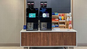 A coffee station with two coffee machines and a shelf with various items.