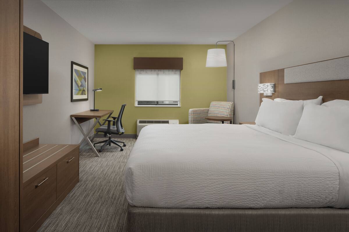 A hotel room with a large bed, a desk, a chair, a television, and a window with curtains.