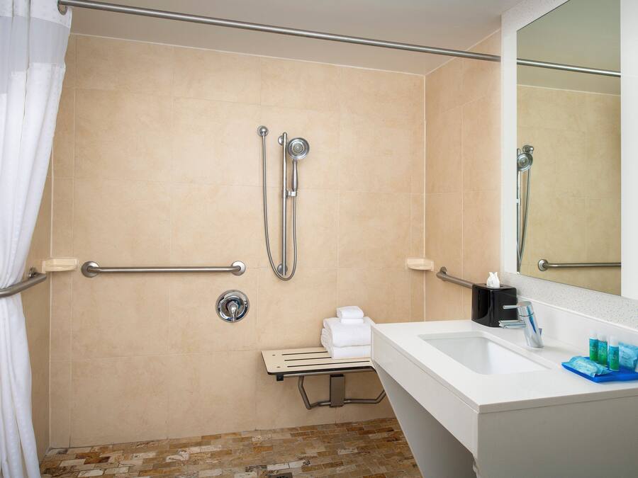 A bathroom with a shower, grab bars, a sink, and a mirror.