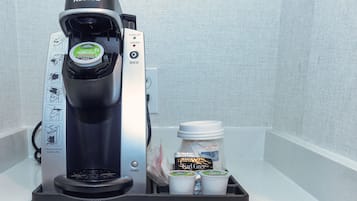 A Keurig coffee maker with a drip tray, a jar of Earl Grey tea, and two disposable cups.