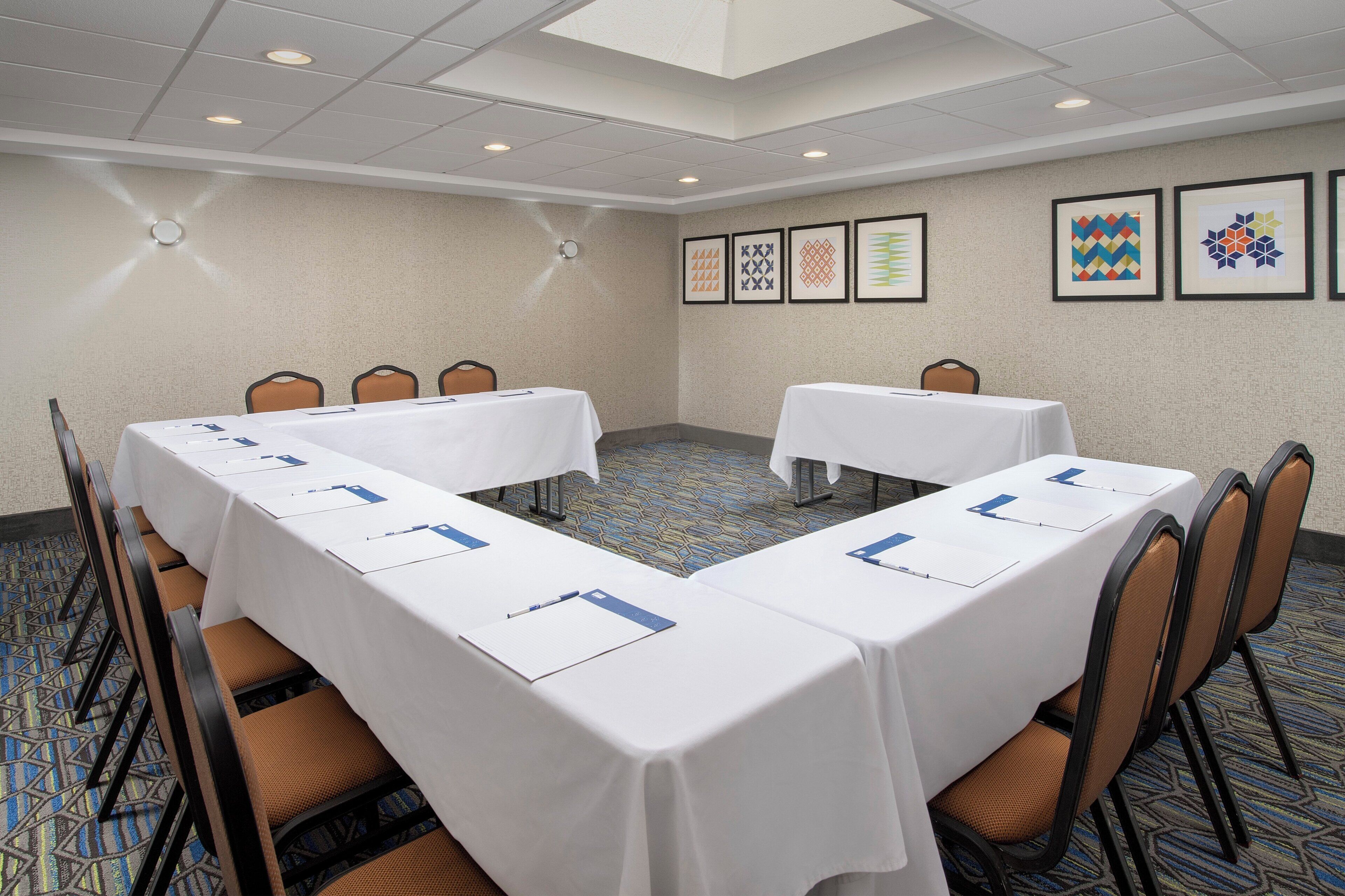 A conference room with two long tables, chairs, and framed artwork on the walls.