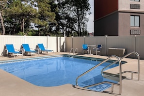 A swimming pool with blue water, surrounded by white fences and blue lounge chairs.